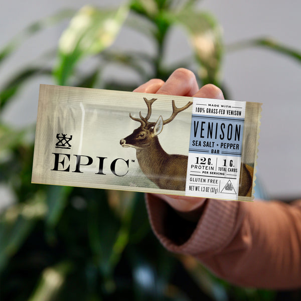 A hand holding EPIC's Grassfed Venison Sea Salt Pepper Bar close up to the camera. 